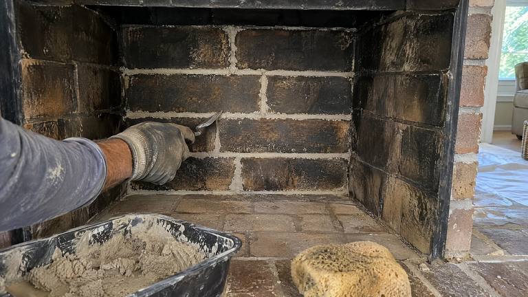 Fresh light gray refractory mortar joints stand out between soot-darkened firebricks in a repaired firebox.