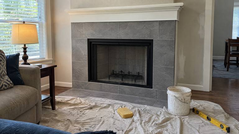 A newly installed wood-burning fireplace in a fresh tile surround, with a drop cloth and tools still on the floor.