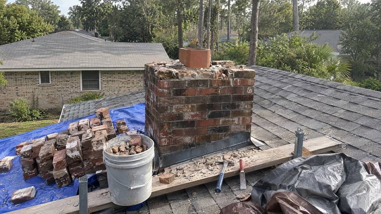 A brick chimney taken down close to the roof, with salvaged bricks stacked on a blue tarp beside it.