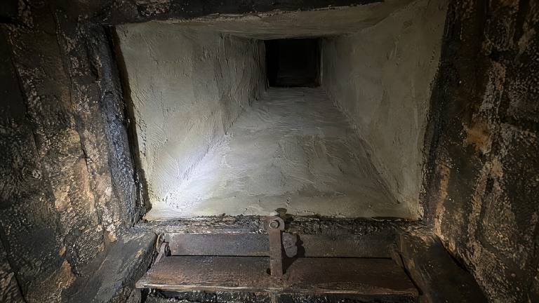 Looking up inside a fireplace at a freshly parged, smooth gray smoke chamber lit by a flashlight.