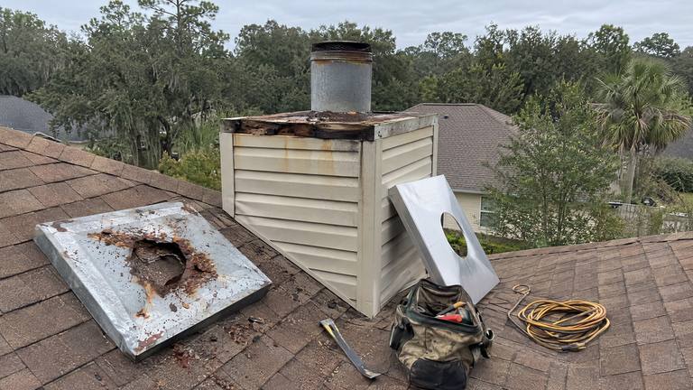 An old rusted chase cover lies on the roof beside a sided chimney chase, with a new cover leaning against it.